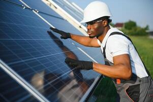 retrato de africano americano electricista ingeniero en la seguridad casco y uniforme instalando solar paneles foto