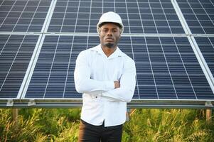 Close up portrait of young handsome African American craftsman a protective helmet. Happy man in overalls posing at camera smiling. Slow motion. photo