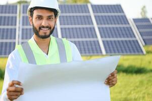 masculino árabe ingeniero en pie en campo con filas de solar paneles foto