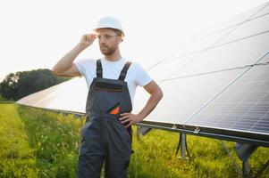 Side view of male worker installing solar modules and support structures of photovoltaic solar array. Electrician wearing safety helmet while working with solar panel. Concept of sun energy photo