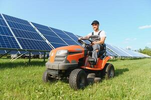 A man drives a lawnmower near solar panels. Concept of solar energy photo