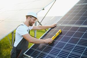 Side view of male worker installing solar modules and support structures of photovoltaic solar array. Electrician wearing safety helmet while working with solar panel. Concept of sun energy photo