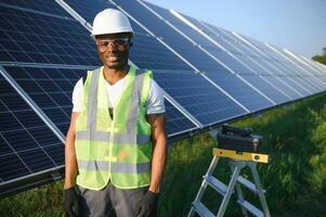 retrato de africano americano electricista ingeniero en la seguridad casco y uniforme instalando solar paneles foto