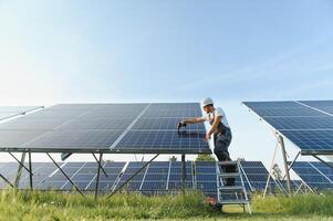 Side view of male worker installing solar modules and support structures of photovoltaic solar array. Electrician wearing safety helmet while working with solar panel. Concept of sun energy photo