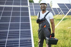 retrato de africano americano electricista ingeniero en la seguridad casco y uniforme instalando solar paneles foto