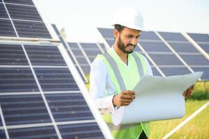 An Indian male engineer in a green vest is working on a field of solar panels. The concept of renewable energy. photo