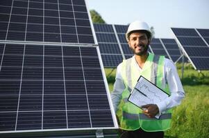 Male arab engineer standing on field with rows of solar panels. photo