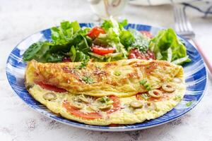 Omelette with tomatoes, green olives and fresh salad on blue plate.  Frittata - italian omelet. photo