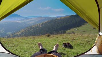 The man stand near the tent on the background of mountain landscape. He enjoys nature in his journey. 4K video