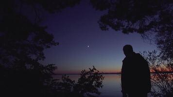 Dark night lonely man with a lamp stands on the banks of the river video