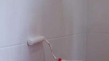 La peinture carrelage dans le cuisine dans le salle de bains, blanc peindre avec une rouleau. main dans gant avec rouleau proche en haut ralenti vidéo 4k video
