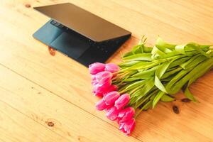 A bouquet of pink tulips flowers on a background of boards with an open laptop. photo
