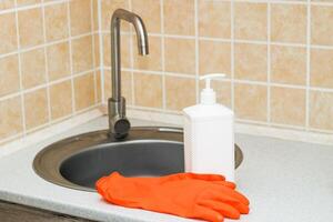 Kitchen sink with faucet and gloves for cleaning and detergent. photo