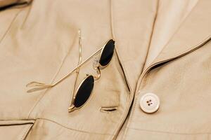 Gold-rimmed sunglasses on the texture of a brown leather jacket, genuine soft leather photo