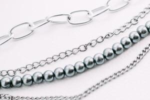 A necklace of gray beads with chain decorations on a white aesthetic background. photo