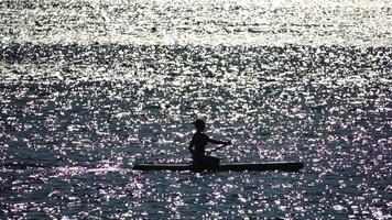 hav kvinna supera. silhuett av Lycklig positiv ung kvinna i bikini, surfing på supera styrelse, självsäker paddling genom vatten yta. idyllisk solnedgång. aktiva livsstil på hav eller flod. långsam rörelse video