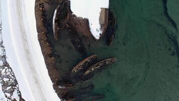 Top view of many old wrecked ships drowned at the sea shore in snowy winter season. Footage. Aerial view of the ruined boats in the cold water near snowy coast. video