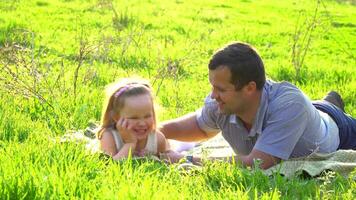 padre e figlia menzogna su il verde erba. essi siamo contento e sorridente. felicità e armonia nel famiglia vita. contento famiglia concetto. video