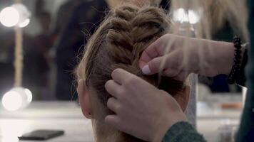 Hairdresser makes pigtails to a girl. Young girl gets a beautiful hairstyle. Close up video