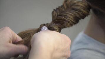 Hairdresser makes pigtails to a girl. Young girl gets a beautiful hairstyle. Close up video