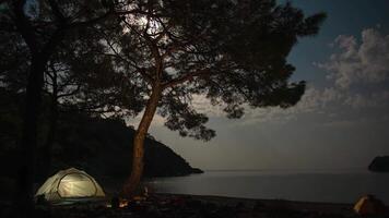 Time lapse of Clouds and the moon move over the bay and tent on the shores of the Mediterranean Sea. Freedom and travel concept. Zoom out. video