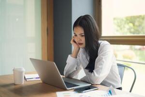 A woman is sitting at a desk with a laptop and a cup of coffee. She is deep in thought, possibly working on a project or dealing with a personal issue. Concept of focus and concentration photo
