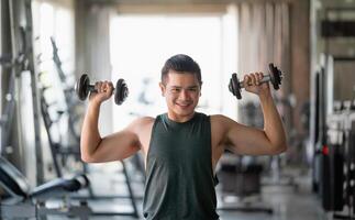 Asian sport man using dumbbell exercise at gym. Asian body building for muscle training. Sport health gym concept. photo