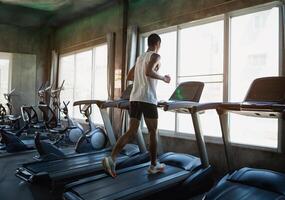 Back side of asian sportman runner running on treadmill in fitness club. Cardio workout. Healthy lifestyle, guy training in gym. Sport running concept. photo