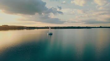 Antenne Aussicht einer Yacht beim Sonnenuntergang im das öffnen Meer. Flug beim Sonnenuntergang in der Nähe von das Yacht mit ein segeln Aussicht von ein Höhe. das Sonne ist reflektiert im das Wasser. video