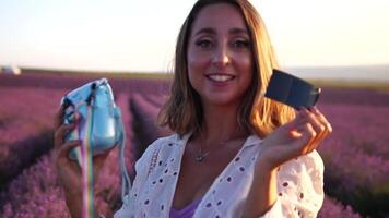 Smiling happy woman photographing with instant camera in lavender field on sunny day. Young woman shooting with blue instant camera - Trendy girl taking selfie outdoor video