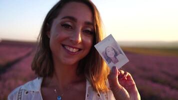 Smiling happy woman photographing with instant camera in lavender field on sunny day. Young woman shooting with blue instant camera - Trendy girl taking selfie outdoor video