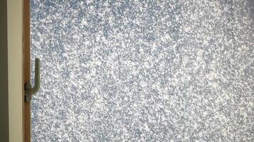 Wet snow falls on the glass melts and flows a drop down on a window at Christmas time. Snowflakes and crystals are melting against blue sky. Cold wet weather on window pane. Weather and climate change video