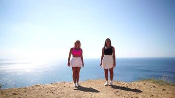 Woman summer travel sea. Two happy carefree ladies raise their hands on the rock of the sea ocean. Sunny day, capturing triumph and admiration of breathtaking view, celebrating achievement. video