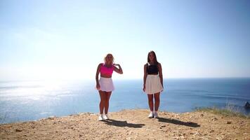 Woman summer travel sea. Two happy carefree ladies raise their hands on the rock of the sea ocean. Sunny day, capturing triumph and admiration of breathtaking view, celebrating achievement. video