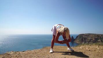 mujer mar aptitud física. contento rubia mujer, aptitud instructor en ropa de deporte haciendo extensión y pilates en acantilado terminado el mar. hembra aptitud yoga rutina concepto. sano estilo de vida. video