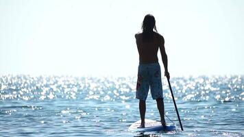 homem sup mar. Forte Atlético homem aprende para remo sup em pé em borda dentro aberto mar oceano em ensolarado dia. verão feriado período de férias e viagem conceito. aéreo visualizar. lento movimento video