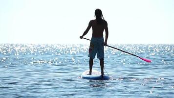 Mens sup zee. sterk atletisch Mens leert naar peddelen sup staand Aan bord in Open zee oceaan Aan zonnig dag. zomer vakantie vakantie en reizen concept. antenne visie. langzaam beweging video