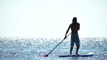 Man Sup Sea. Strong athletic man learns to paddle sup standing on board in open sea ocean on sunny day. Summer holiday vacation and travel concept. Aerial view. Slow motion video