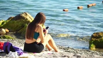 vrouw met smartphone. vrouw Holding verticaal mobiel telefoon en vegen omhoog door vinger toepassing bladzijde tegen achtergrond van zee en strand video