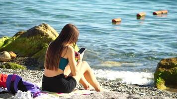 donna con smartphone. donna Tenere verticale mobile Telefono e strisciare su di dito applicazione pagina contro sfondo di mare e spiaggia video