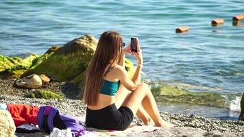 donna con smartphone. donna Tenere verticale mobile Telefono e strisciare su di dito applicazione pagina contro sfondo di mare e spiaggia video