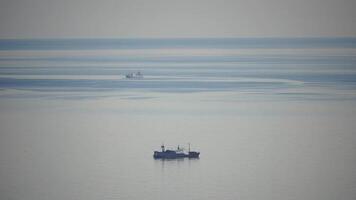 Fishing boat trawler catches fish while sailing on sea. A commercial fishing boat on the horizon in a distance sail to catch school of fish on calm sea surface in summer. Commercial catch of sea fish. video