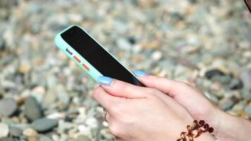 Woman with smartphone. Close-up of woman's hands holding vertical mobile phone and swiping up finger application page against background of sea and beach video