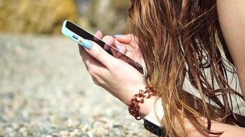 Woman with smartphone. Close-up of woman's hands holding vertical mobile phone and swiping up finger application page against background of sea and beach video