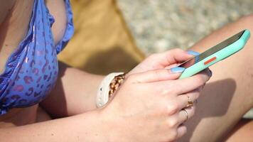 Woman with smartphone. Close-up of woman's hands holding vertical mobile phone and swiping up finger application page against background of sea and beach video