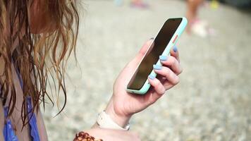 Woman with smartphone. Close-up of woman's hands holding vertical mobile phone and swiping up finger application page against background of sea and beach video