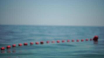 Abstract defocused orange safety buoys on a rope floating in the sea on a sunny day. Fencing of the swimming area on the beach. video