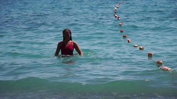 Jeune femme avec longue cheveux dans une rouge maillot de bain et bracelets dans boho style profiter le vagues sur le plage dans été. adorable content féminin relaxant à été plage ayant vacances. lent mouvement. video