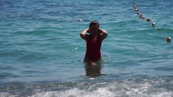 jung Frau mit lange Haar im ein rot Badeanzug und Armbänder im Boho Stil genießen das Wellen auf das Strand im Sommer. bezaubernd glücklich feminin entspannend beim Sommer- Strand haben Urlaub. schleppend Bewegung. video