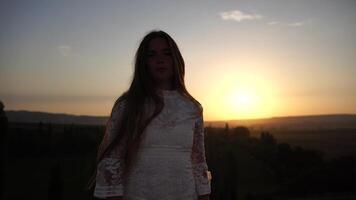 contento donna nel bianca boho vestito su tramonto nel montagne. romantico donna con lungo capelli in piedi con sua indietro su il tramonto nel natura nel estate con Aperto mani. silhouette. natura. tramonto. video